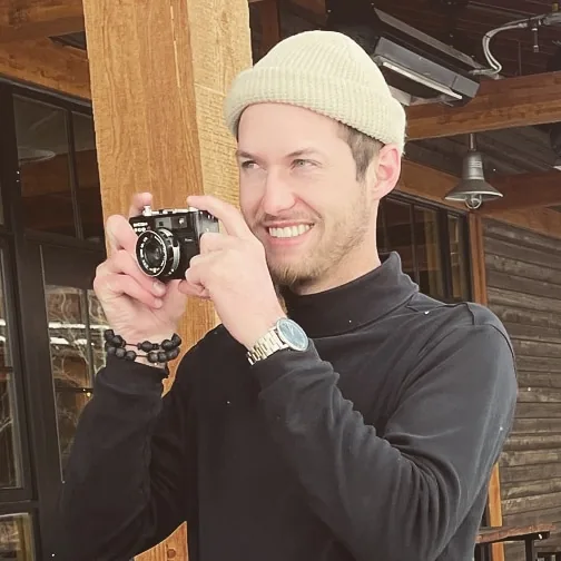 Adrian Hallberg, founder of Kindred, smiling and holding a film camera